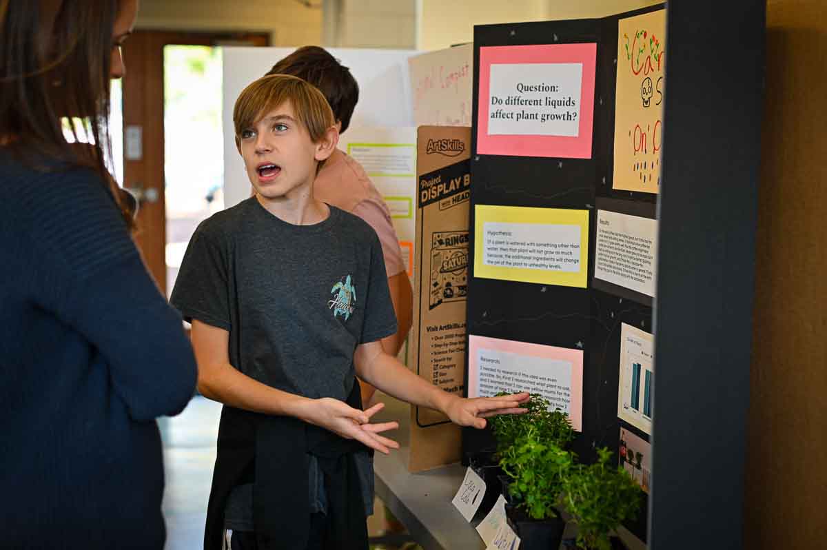 Private middle school student explains science project to parent at homeschool coop.