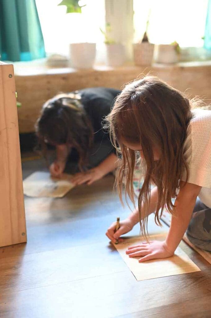 Two girls write on worksheet while leaning on floor at homeschool coop.