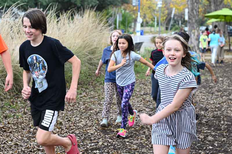 Progressive school students run outdoors by grassy area.