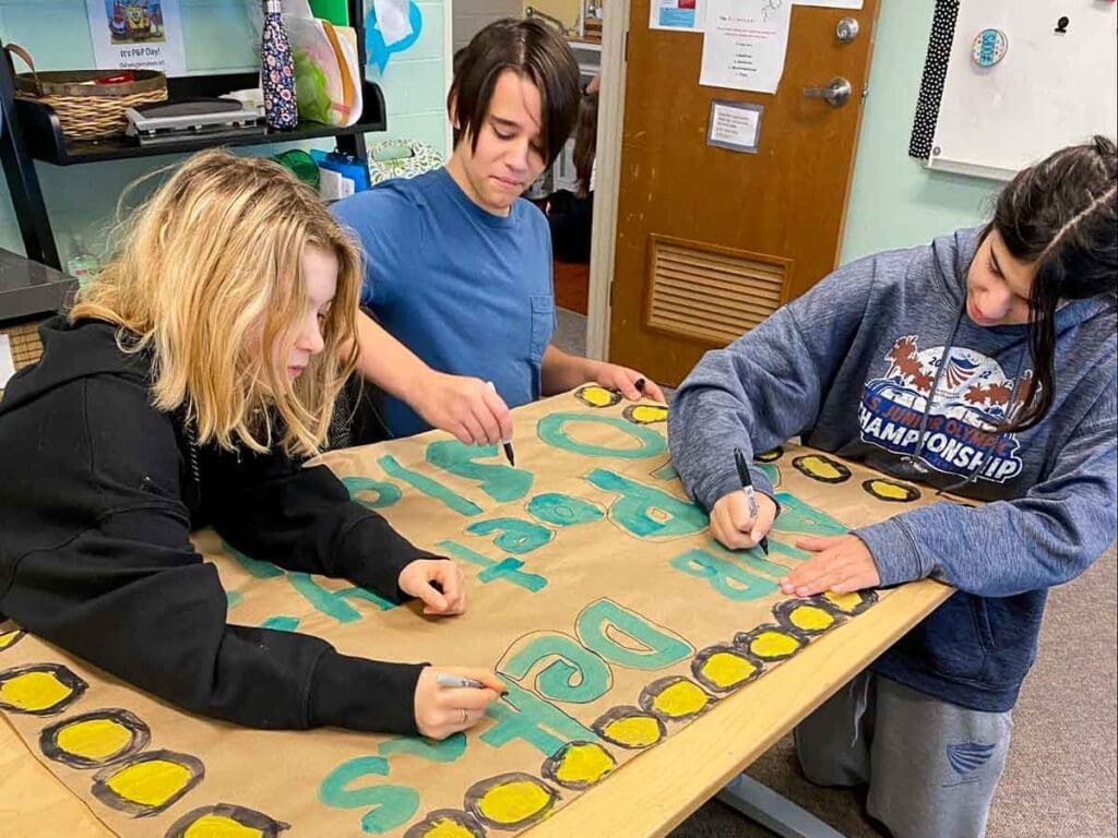 Three middle schoolers work on poetry poster at non traditional school.